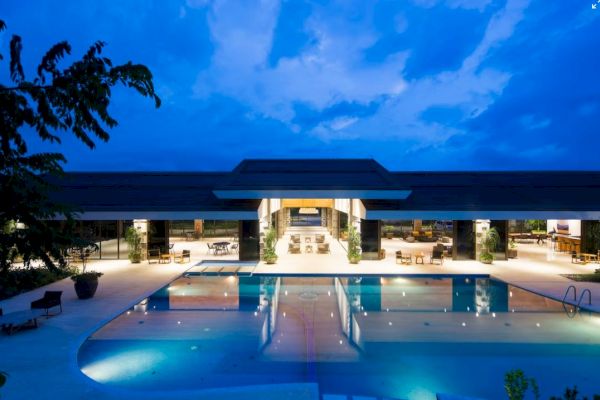 A luxurious building with a large swimming pool illuminated at night, lounge chairs around, and a partly covered area with seating.