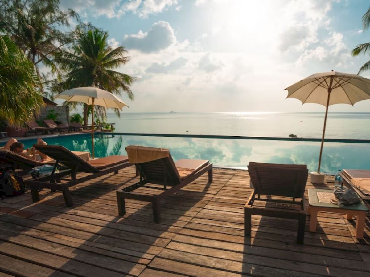 A serene poolside scene with lounge chairs, umbrellas, and a stunning ocean view under a partly cloudy sky.
