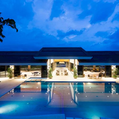 The image shows a luxurious building with a pool in front, illuminated at dusk, reflecting a serene ambiance.