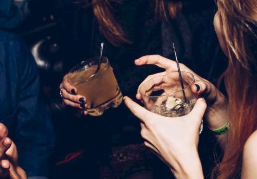 People are joyfully socializing, holding drinks, and laughing in a dimly lit environment, likely at a party or a bar.