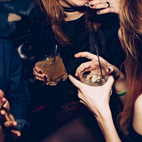 People are joyfully socializing, holding drinks, and laughing in a dimly lit environment, likely at a party or a bar.
