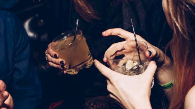 People are joyfully socializing, holding drinks, and laughing in a dimly lit environment, likely at a party or a bar.