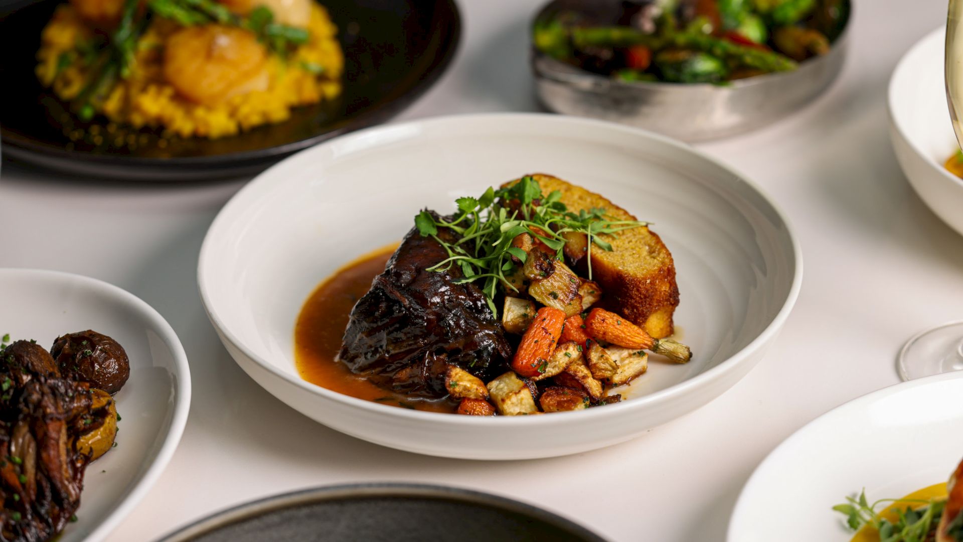 A variety of dishes including meat, vegetables, and garnishes are artfully plated on a table.
