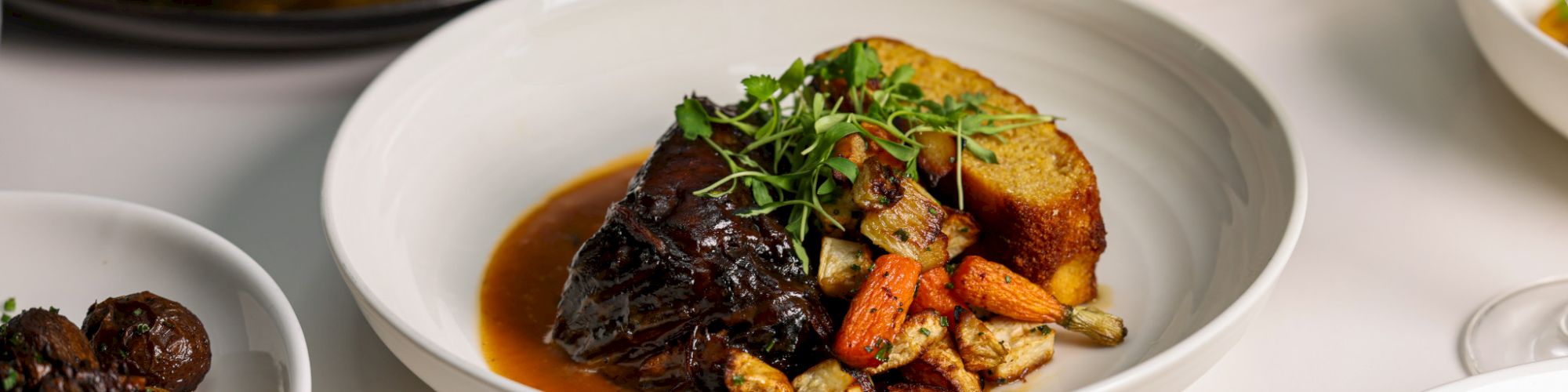 A variety of dishes including meat, vegetables, and garnishes are artfully plated on a table.