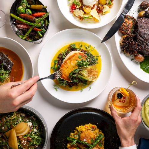 An elegant spread of diverse gourmet dishes including steak, fish, vegetables, salad, and mashed potatoes, alongside drinks and a dessert.