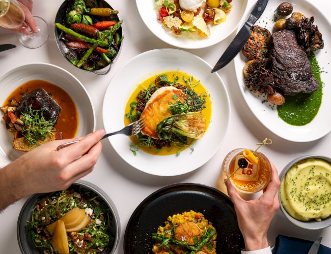 An elegant spread of diverse gourmet dishes including steak, fish, vegetables, salad, and mashed potatoes, alongside drinks and a dessert.