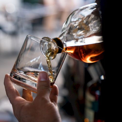 A close-up of a hand pouring a golden liquid, likely whiskey, from a bottle into a glass.