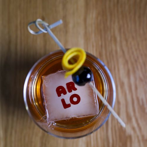 A cocktail glass with an ice cube displaying the letters 