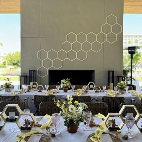 A beautifully set dining table with yellow accents and floral arrangements against a hexagonal wall design backdrop.