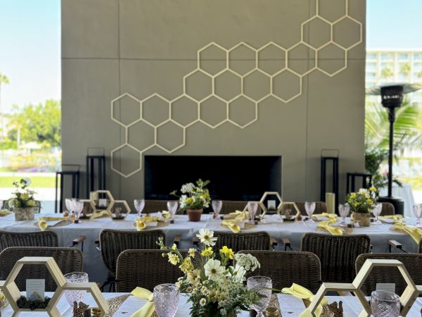 A decorated dining setup with yellow napkins, hexagonal frames, and floral centerpieces in an outdoor space with hexagon wall art.