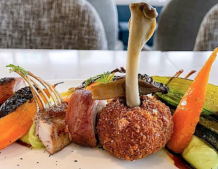 A gourmet dish featuring a variety of vegetables, meats, and what appears to be a mushroom centerpiece presented in an artistic arrangement.