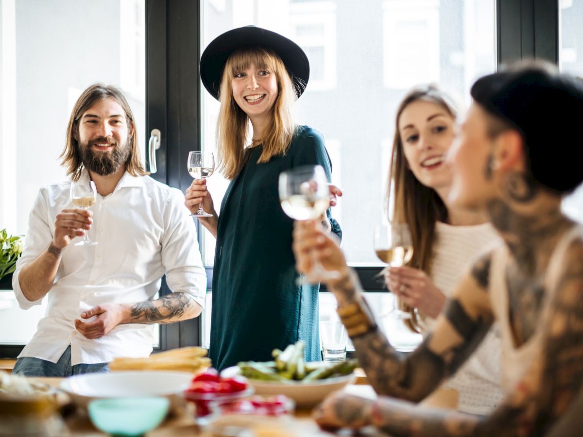 A group of four friends enjoying drinks together, sitting at a table with snacks and smiling warmly.