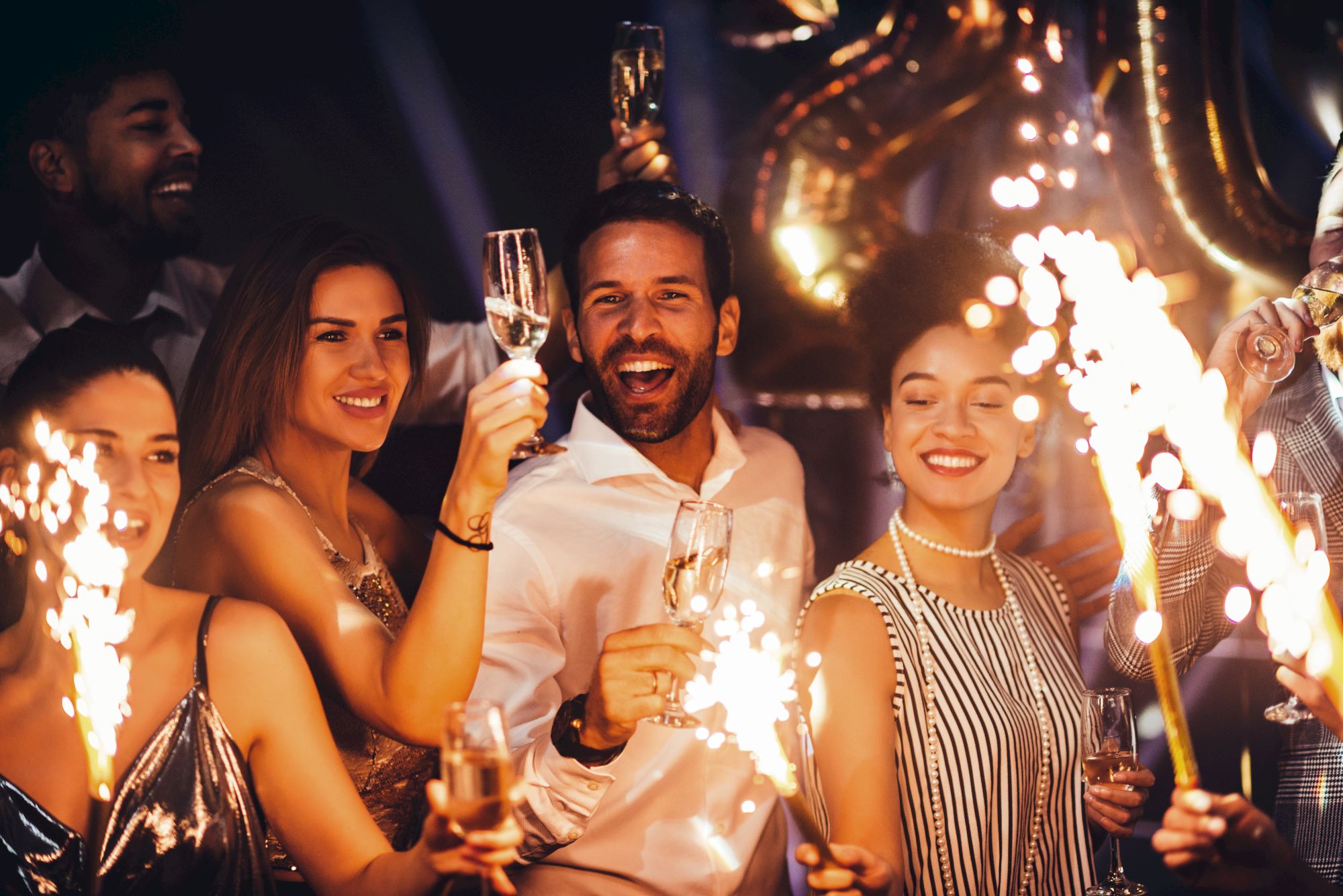 A group of people celebrating with sparklers and champagne, smiling and enjoying a festive atmosphere.