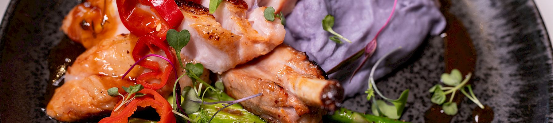 The image shows a plate with grilled salmon, asparagus, purple mashed potatoes, topped with sliced red peppers and microgreens.