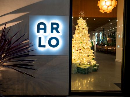 A glowing &ldquo;ARLO&rdquo; sign and a festive indoor scene with a lit Christmas tree and twinkling lights behind a glass door.