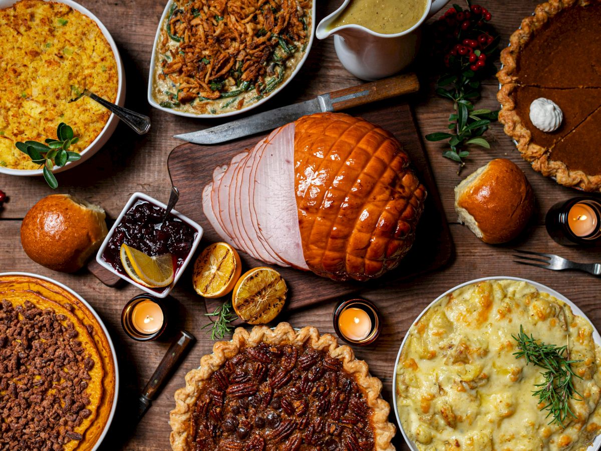 A festive spread with glazed ham, pies and casseroles, plus gravy, bread, gingerbread, and candles on a rustic table.