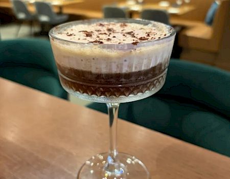 A fancy layered chocolate dessert cocktail in a coupe glass with whipped cream and chocolate shavings on top.