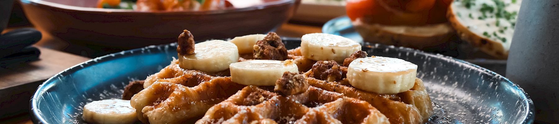 Savory appetizers: fried gnocchi with melted cheese and banana slices on top, plus assorted tapas in the background; wine glass nearby.