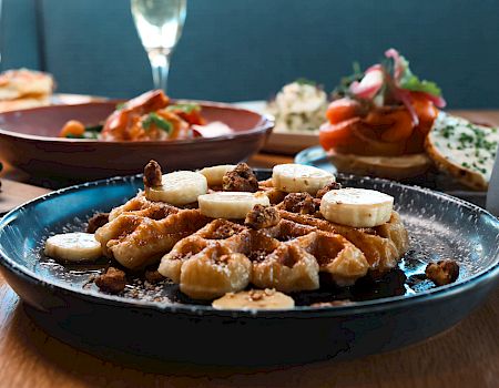 Savory appetizers: fried gnocchi with melted cheese and banana slices on top, plus assorted tapas in the background; wine glass nearby.