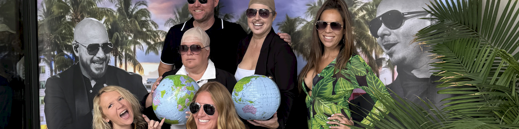 A group of people pose in sunglasses and tropical shirts with globe props before a &ldquo;Dale&rsquo;s Arlo&rdquo; beach-themed backdrop.