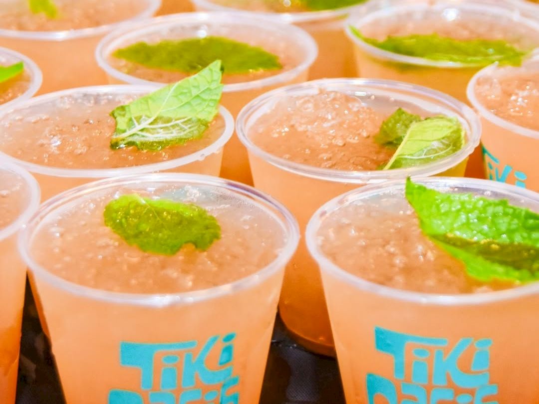 Multiple clear cups of orange juice with green herb leaves floating on top, lined up for a served tasting.