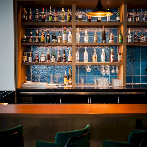 A warmly lit bar shelf lined with liquor bottles and stacked glassware beneath a hanging lamp.