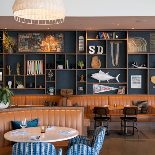 Cozy restaurant interior with wall shelves of decor, a hanging light, and framed posters, including a fish sculpture.