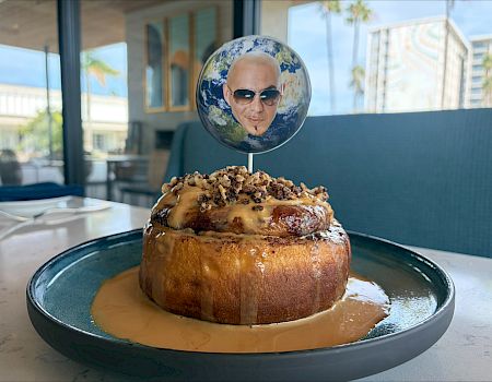 A globe-topped dessert sits on a plate, with caramel sauce drizzled around it in a bright café.