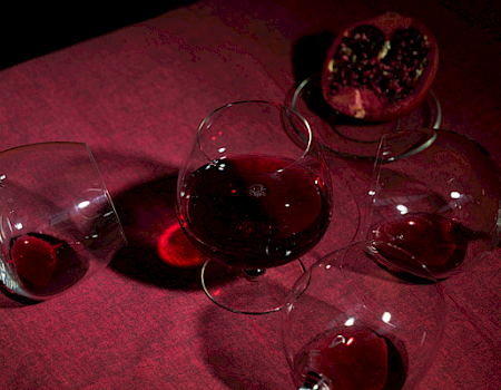 A dark table set with five small glasses of red wine and a garnish bowl under crimson light.