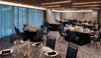 The image depicts an elegantly set dining hall with round tables, black chairs, floral centerpieces, and dim lighting, ready for an event or banquet.