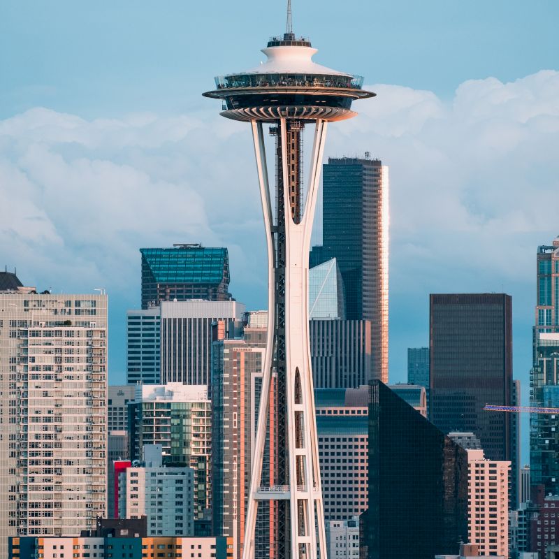 The image shows a skyline with the Space Needle in the center and several surrounding skyscrapers under a partly cloudy sky.