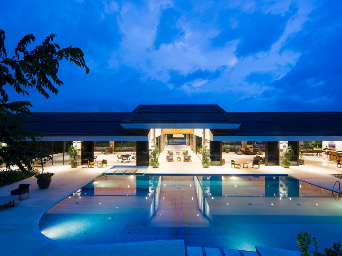 A luxury pool area at night with surrounding open-air seating and a well-lit modern building in the background.