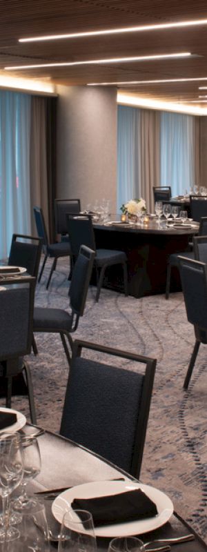 The image shows an elegant banquet hall setup with round tables, black chairs, and place settings, ready for a formal event or dinner.