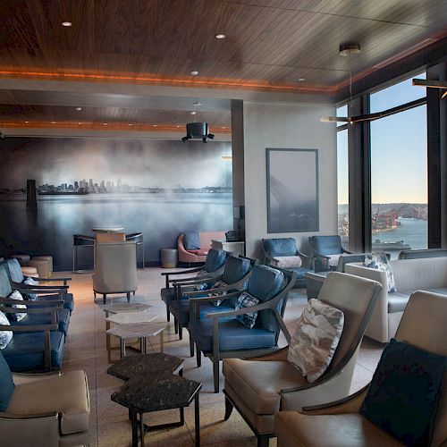 A modern, upscale lounge with comfortable seating and large windows offering a scenic water view and skyline.