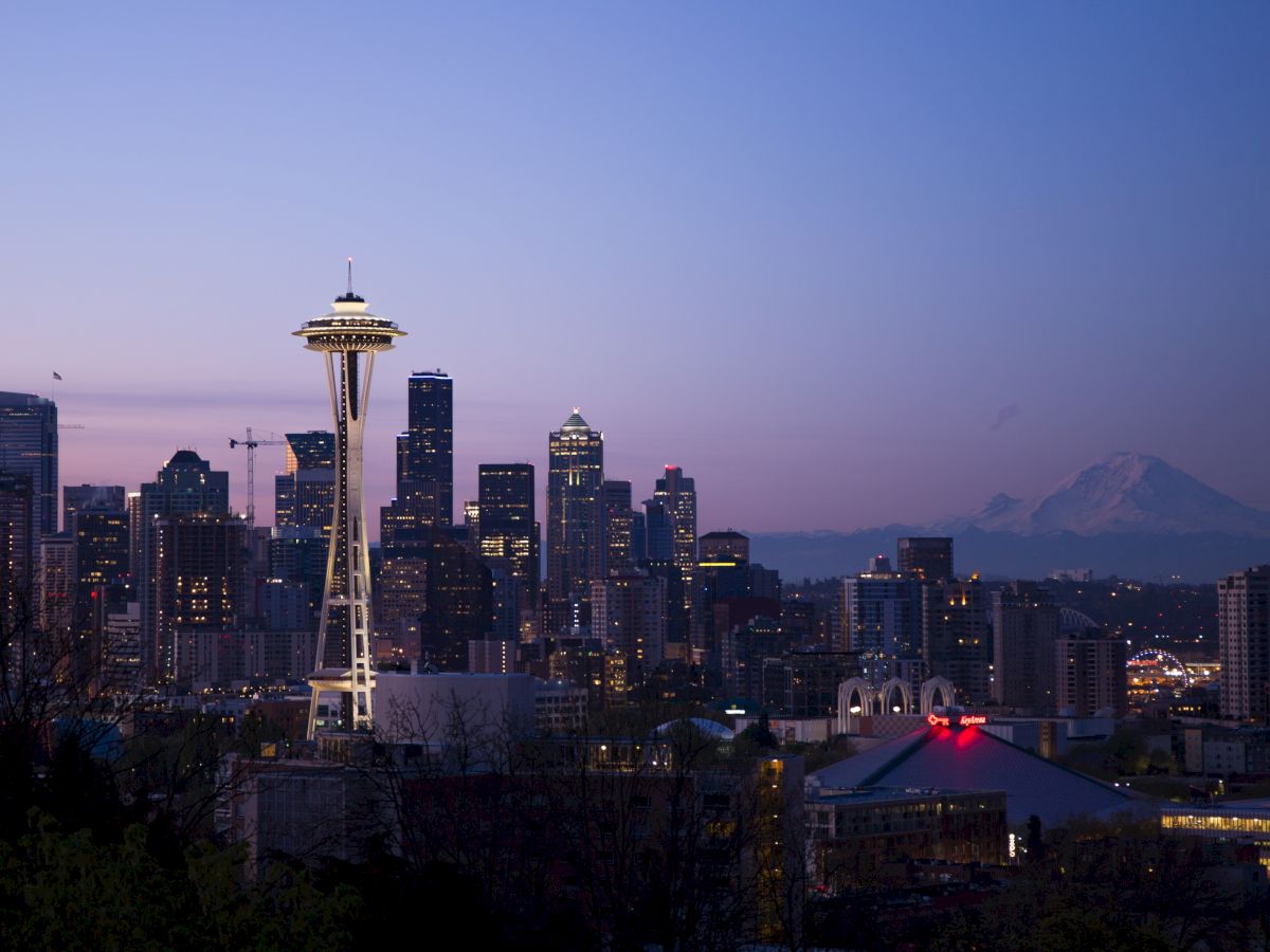 This image shows the Seattle skyline during twilight, featuring the Space Needle and Mount Rainier in the background.
