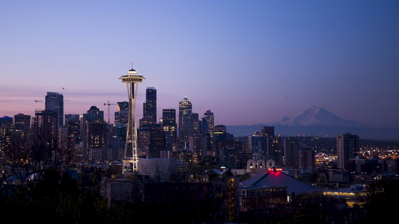 This image shows the Seattle skyline during twilight, featuring the Space Needle and Mount Rainier in the background.